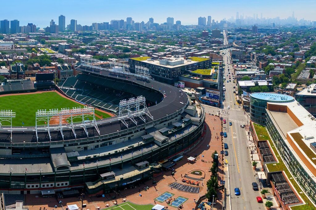 Aerial view of a baseball stadium surrounded by urban buildings and greenery, with a city skyline in the background.
