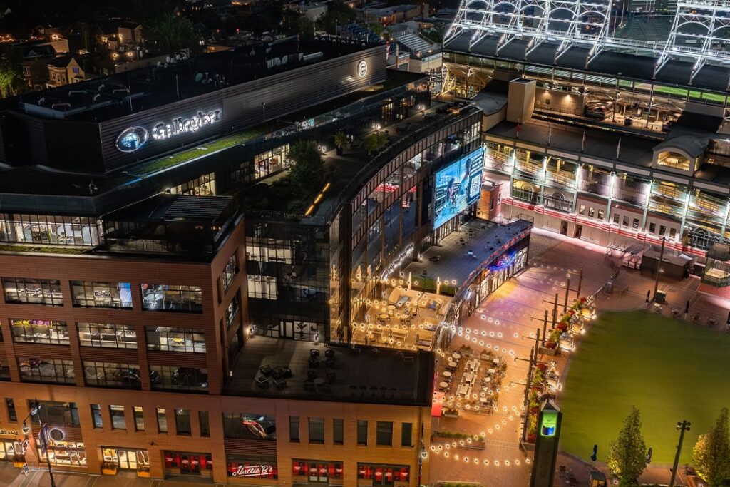 Aerial view of a vibrant Wrigleyville plaza at night, featuring illuminated buildings, outdoor seating, and a large screen.