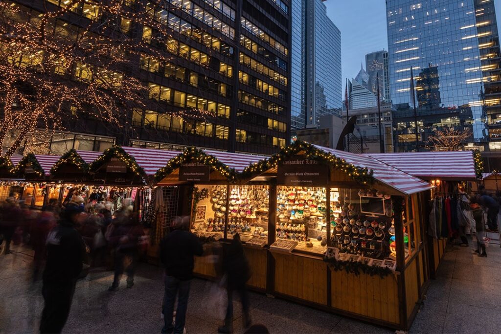 Christmas market stalls with festive garlands among downtown Chicago towers at dusk