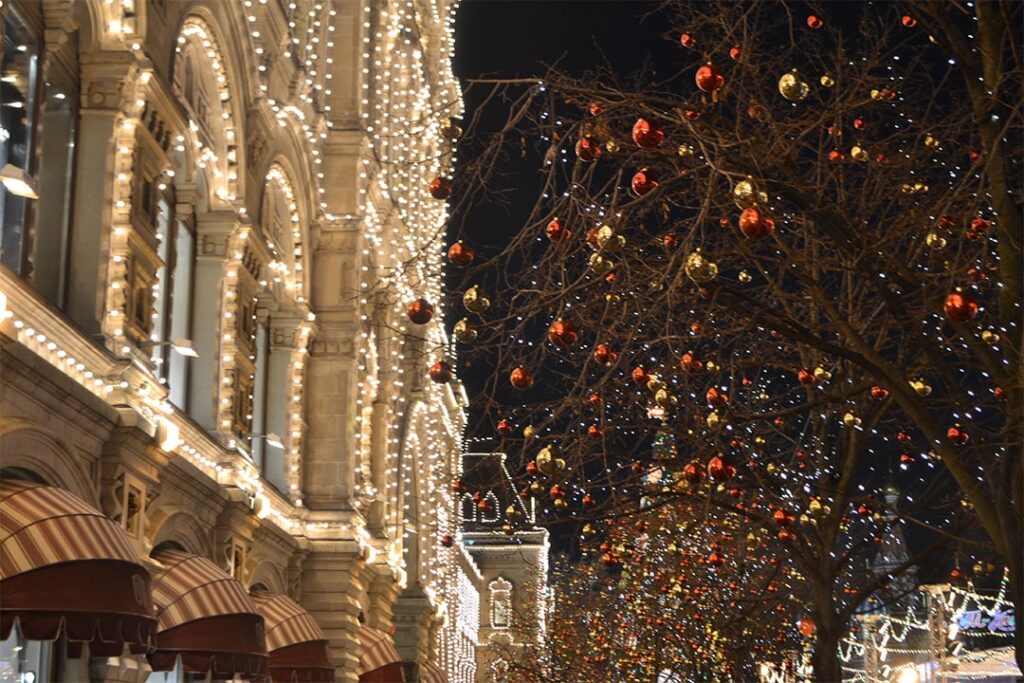 A lit building facade and trees adorned with ornaments lining the sidewalk.