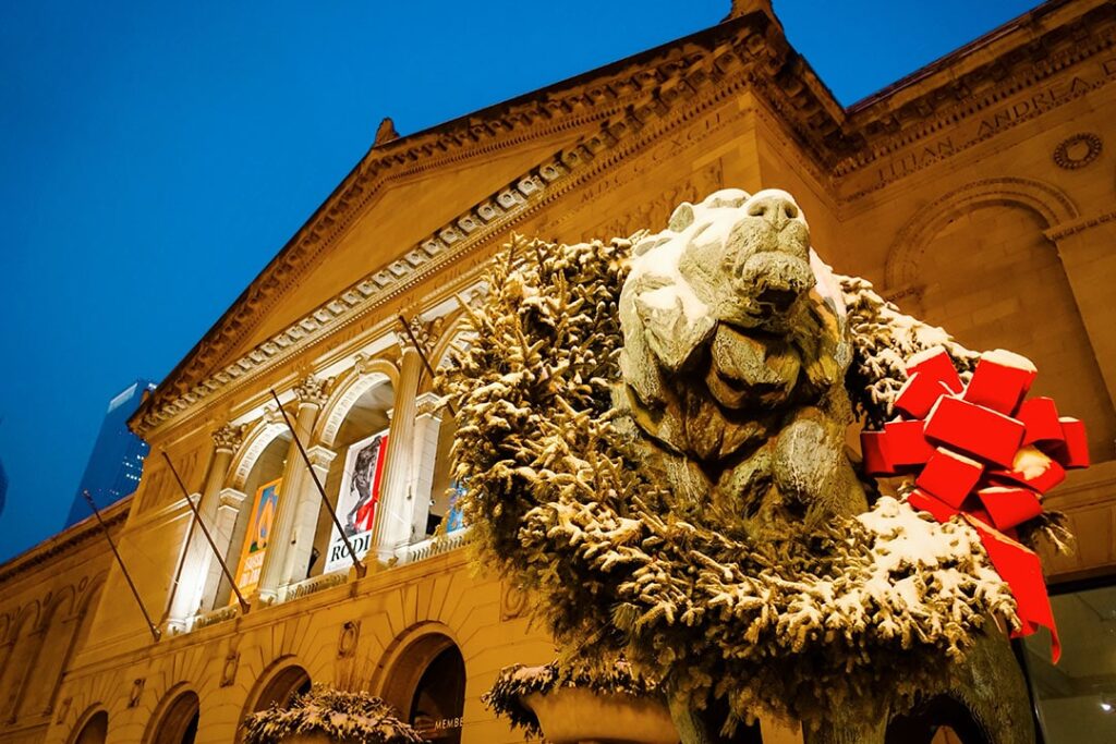 Lion sculpture outside Art Institute of Chicago wearing a snow-dusted holiday wreath and red bow