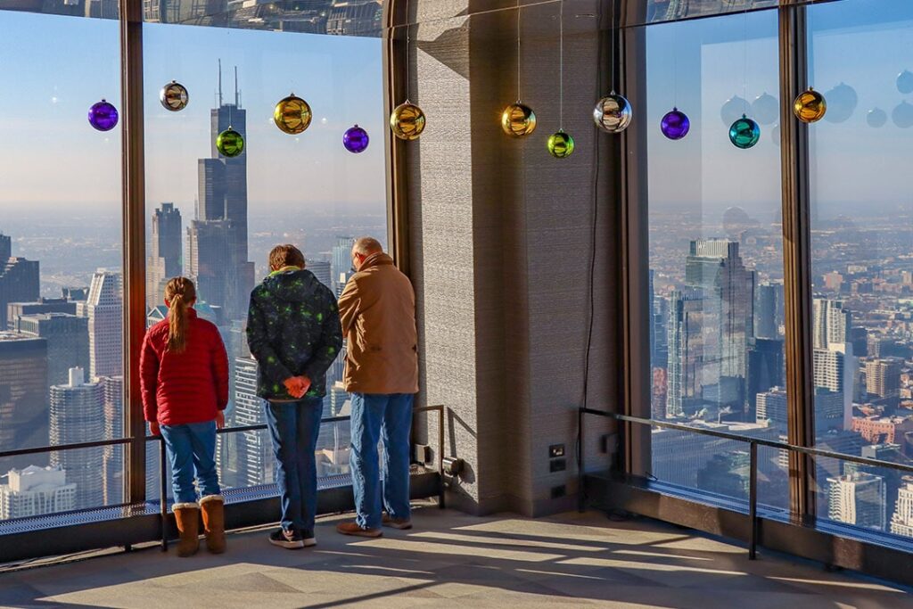 Visitors gaze at the skyline and Willis Tower from 360 CHICAGO, with holiday ornaments hanging in the windows.